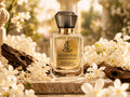 A faceted glass perfume bottle labeled 'Blush Oud' by Royal Essence, styled on a stone surface surrounded by white blossoms and driftwood in a warm, sunlit outdoor setting.